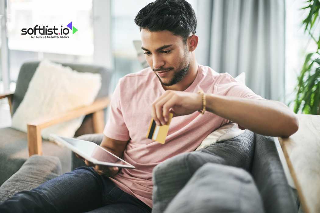 Man holding credit card and using tablet while sitting on sofa