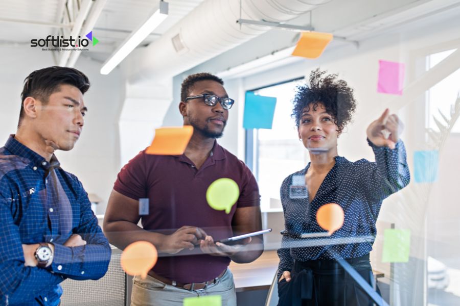 Three colleagues brainstorming with colorful sticky notes on a glass board.