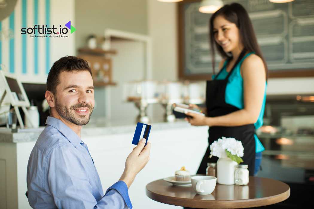 Smiling man holding credit card at cafe table, waitress in background