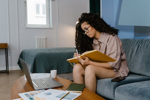 Free A Woman Sitting on Blue Couch Writing on a Notebook Stock Photo