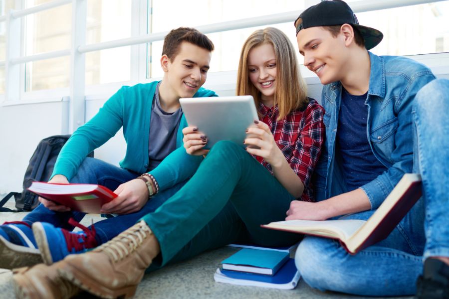 Three students studying together, using a tablet and books.