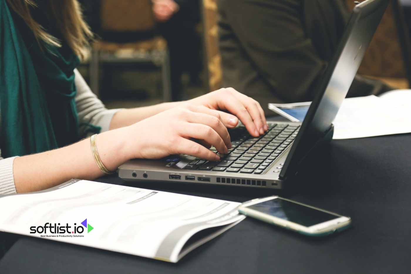 A person typing on a laptop with a smartphone and documents nearby.