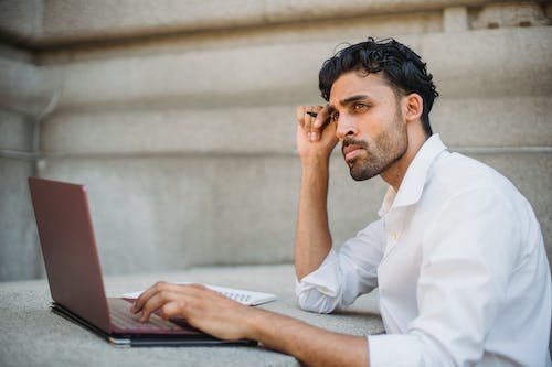 Free Man Sitting at a Table and Working on a Laptop Stock Photo