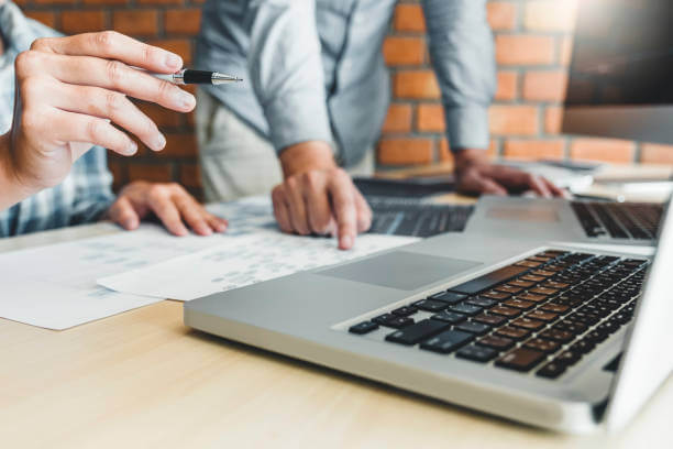 Two people facing their laptop and some papers comparing features