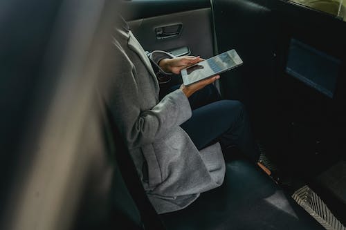 Free Crop unrecognizable female in casual clothes browsing tablet in backseat of modern cab Stock Photo