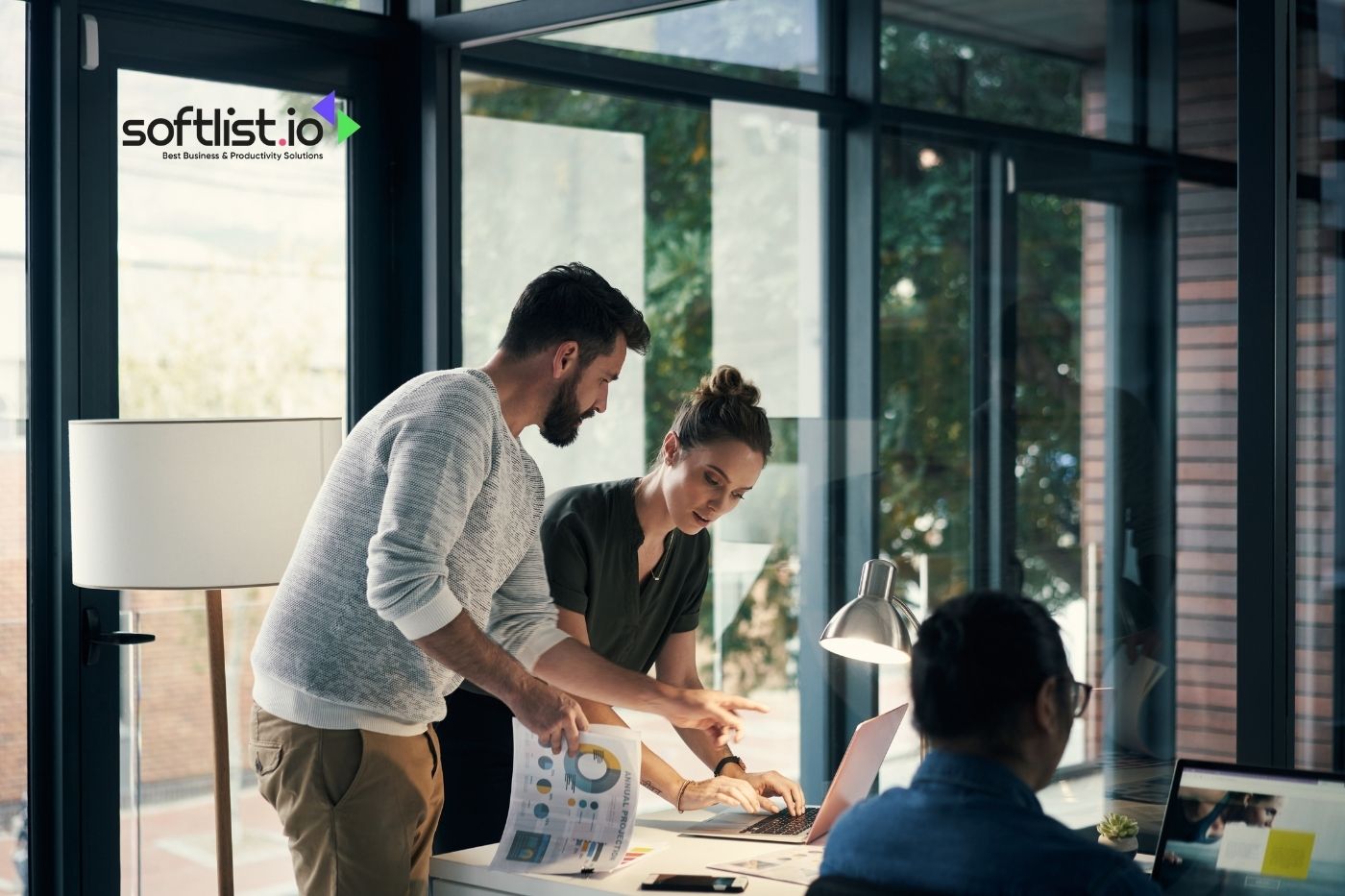 Two professionals discussing over a laptop with softlist.io logo in a well-lit office