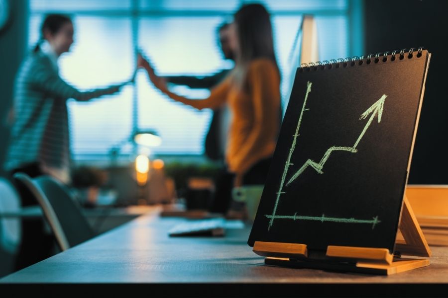 Business people in an office analyzing a graph chart on a blackboard, discussing strategies.