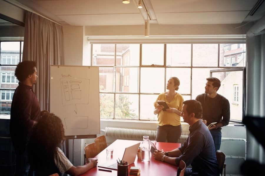 A diverse group of five business professionals in a well-lit, modern office space discussing a presentation.