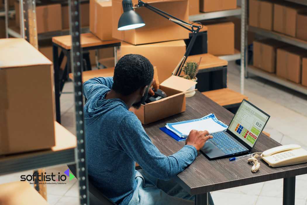 Man working on a laptop surrounded by boxes in a warehouse